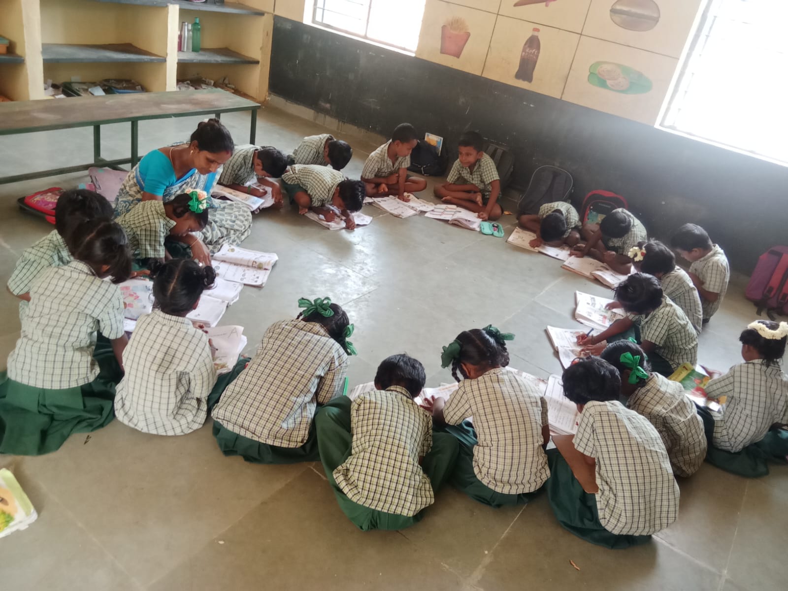 Children and a teacher sitting in a circle on the classroom floor, working in notebooks.